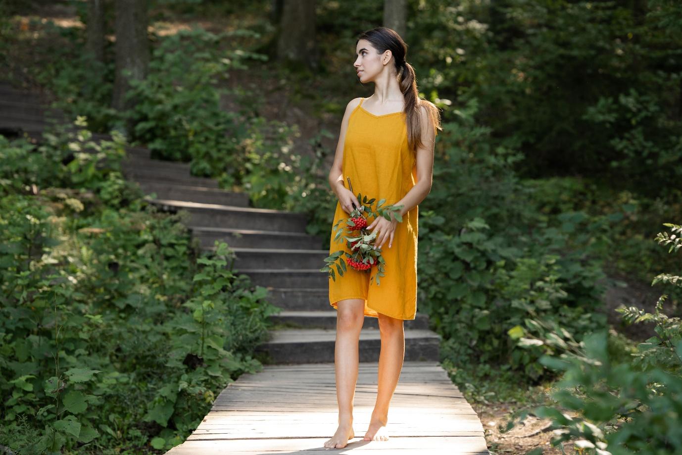 Woman standing in the forest and wearing spicy yellow linen dress.