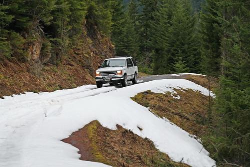 white suv driving on a mountain road with snow on it