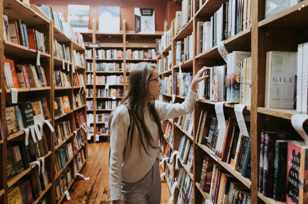 Photograpph of young woman looking through shelves of a bookshop