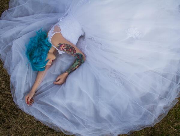 Foto de uma mulher de cabelo azul deitada na grama com a barra do vestido em volta dela 