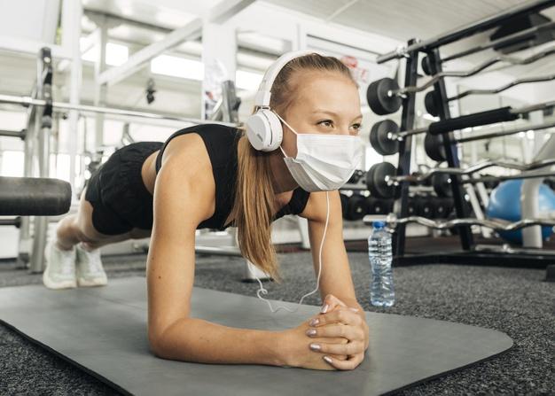 Woman with medical mask and headphones working out at the gym Free Photo