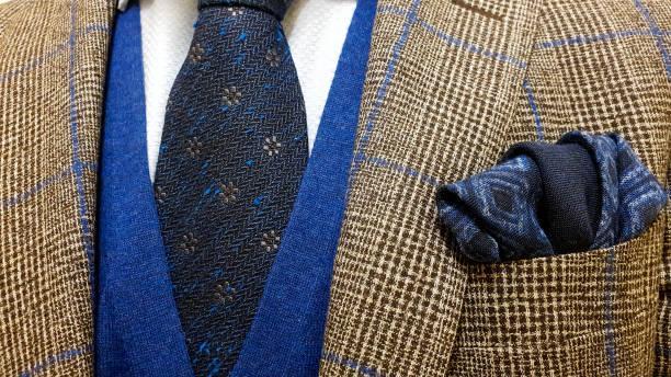 Brown suit jacket with blue squares over a light blue buttoned shirt and a sweater vest together with a matching blue cotton pocket square and a dark blue floral tie Men's fashion concept with a colorful pocket square in a jacket and a matching shirt wool ties stock pictures, royalty-free photos & images