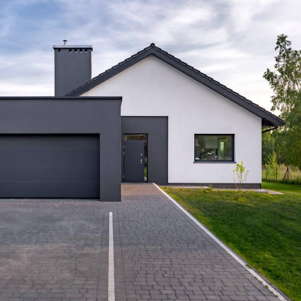 WeServe | a white house with a black front door and garage door with a grey paved driveway and a green front lawn