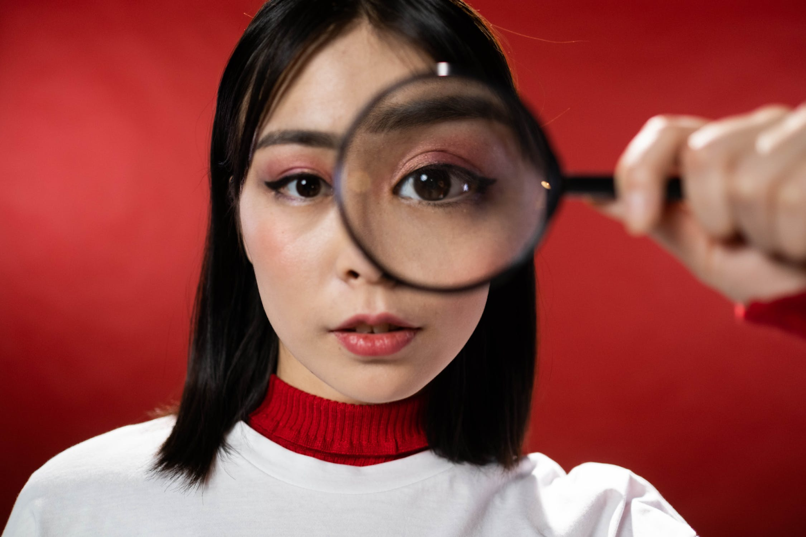 A girl wearing a white and red outfit holding a magnifying glass in front of her face