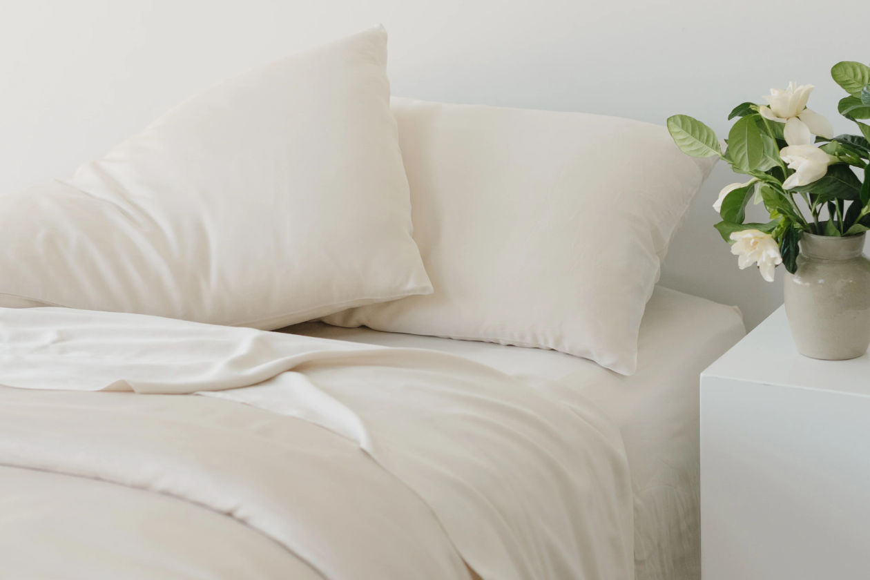 Bed with cream-colored sheets with fresh on the side table.