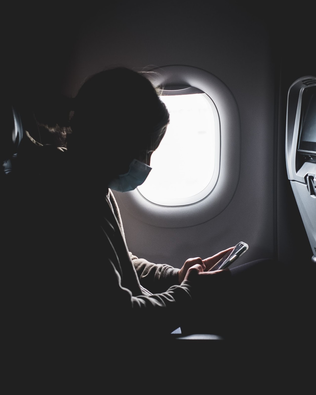 Masked traveler checking phone on a plane