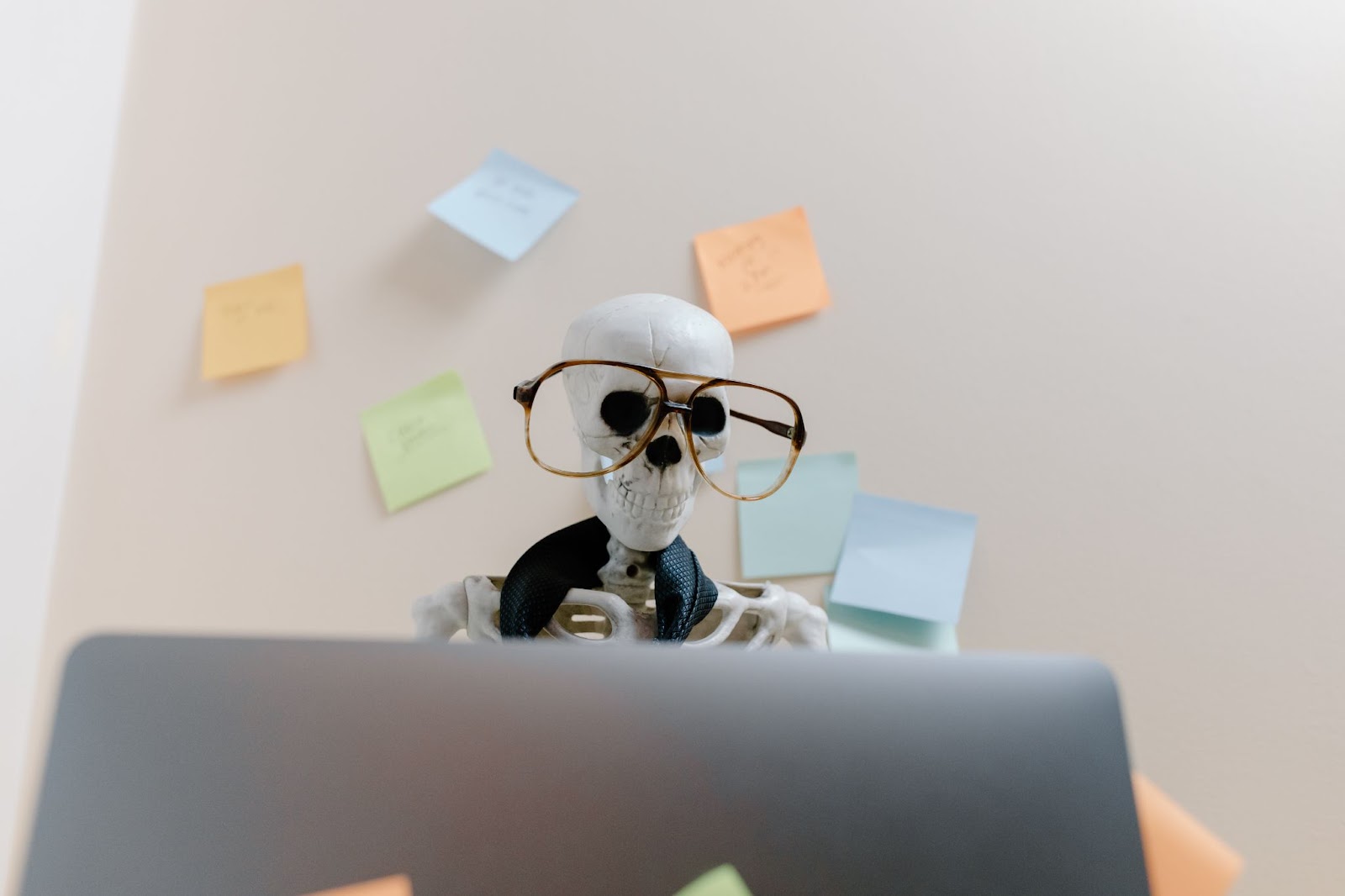 skeleton with glasses looking at a laptop with sticky notes in the background