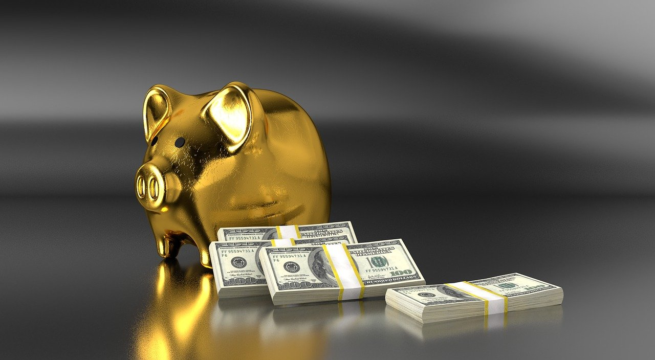 An image of a golden piggy bank with stacks of money next to it. 