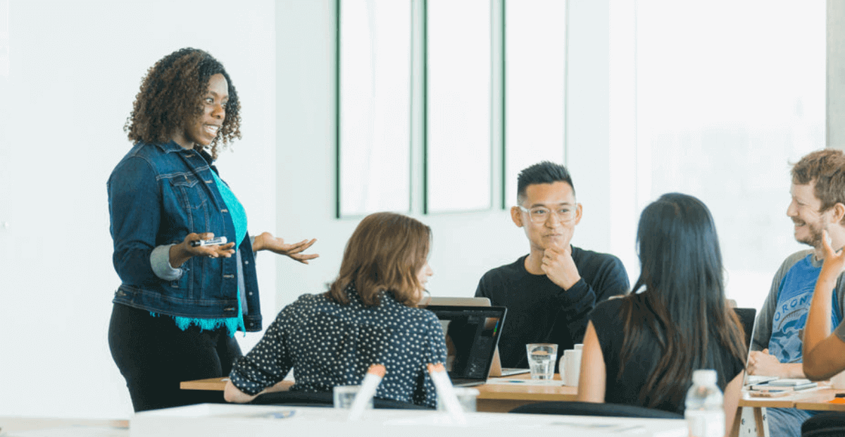 Startups meetings - 1 woman ,standing, while she addresses her seated team members at a startup meeting. 