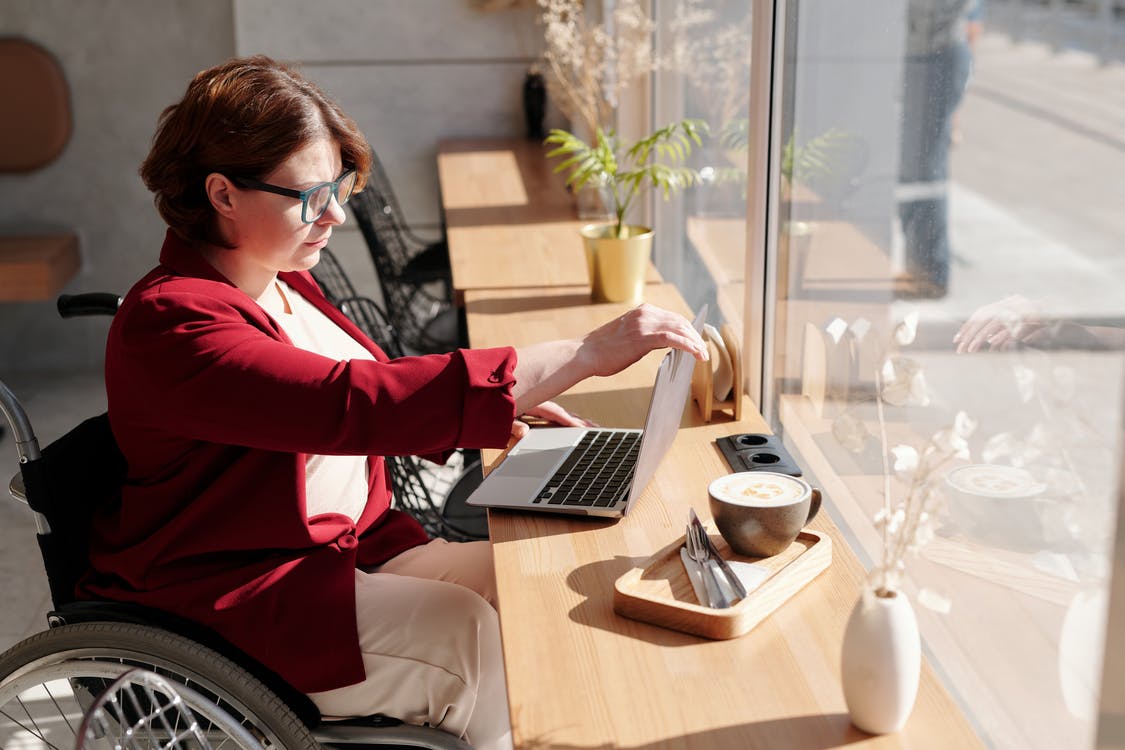 A woman in a wheelchair opening her laptop at a table in a cafe

