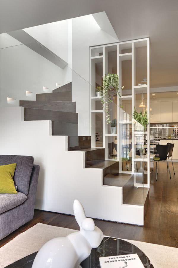 Escada em formato L em dois lances feita na parede casa com estrutura branca, degraus de madeira escura e proteção de vidro