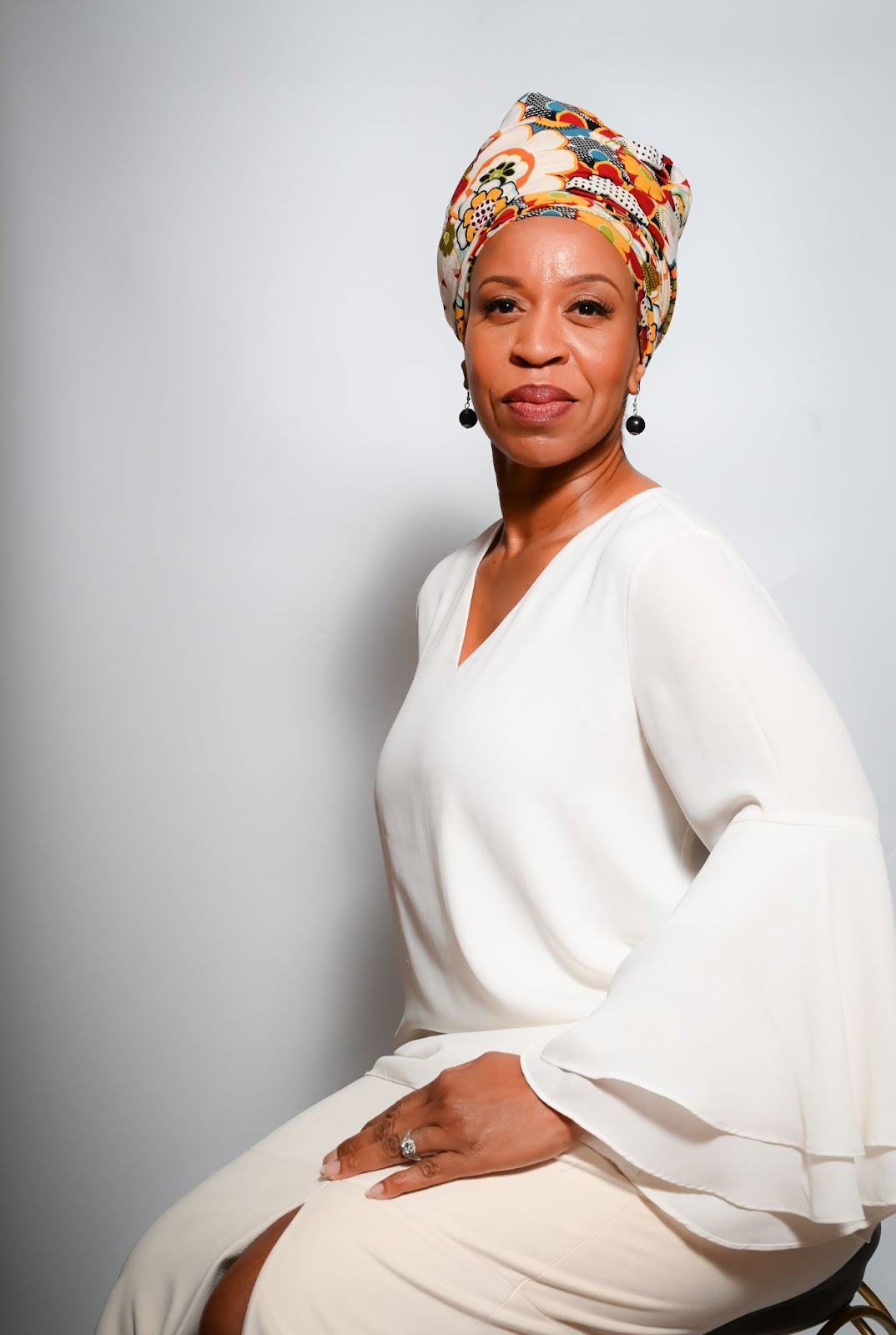 Black woman with a multicolored headwrap and in a white blouse.