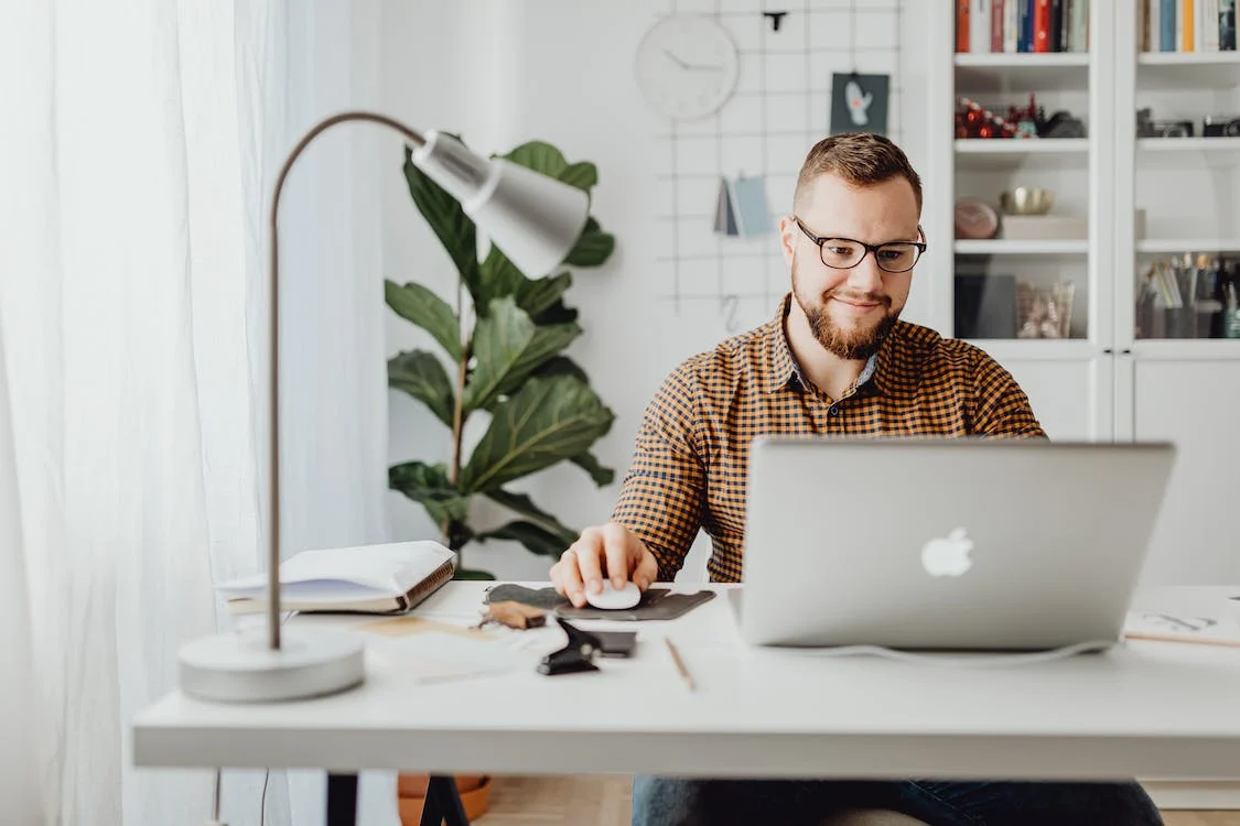 Man wearing glasses using macbook with a mouse