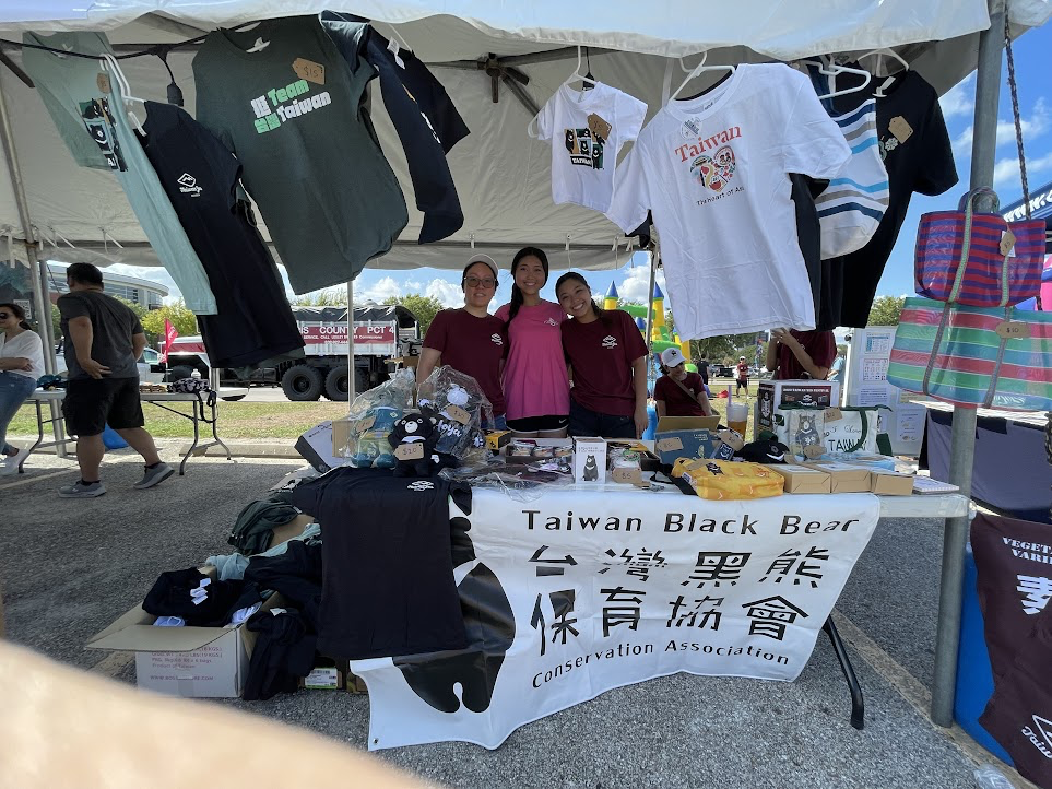 A group of people standing under a tent with t-shirts

Description automatically generated