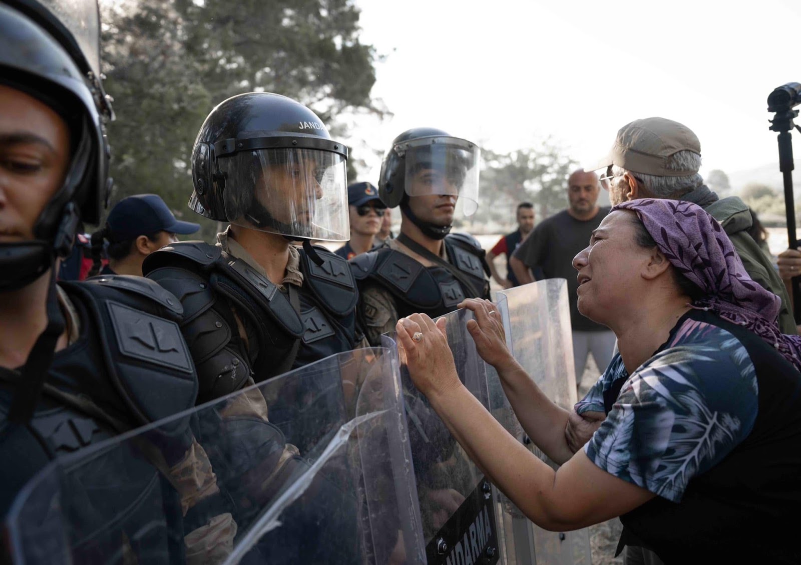 A Turkish villager woman pleads with a stone-faced police officer in riot gear.