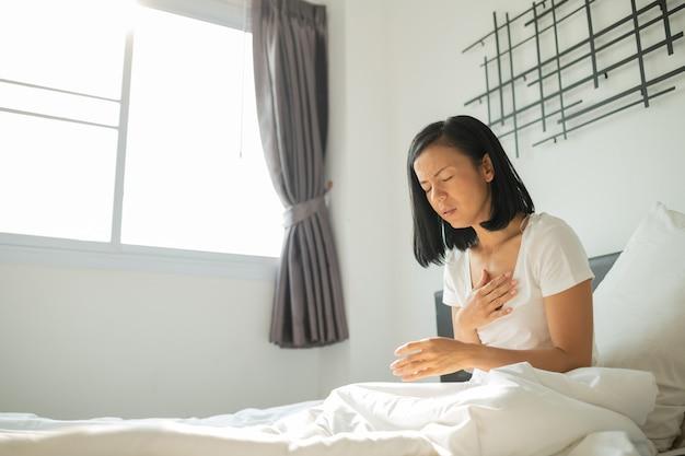 Foto grátis conceito de ataque cardíaco, a mulher asiática não consegue trabalhar, hoje tão cansada. ela está doente, um ataque cardíaco grave e agudo na cama. jovem mulher de pijama, tendo um ataque cardíaco no quarto dela.