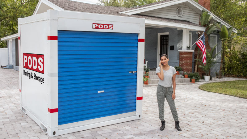 A military servicewoman standing next to a PODS portable moving and storage container in front of her new home