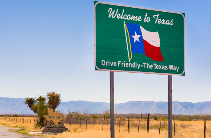 A large sign posted on the side of the road has an image of the Texas state flag and the message, “Welcome to Texas. Drive Friendly - The Texas Way”.