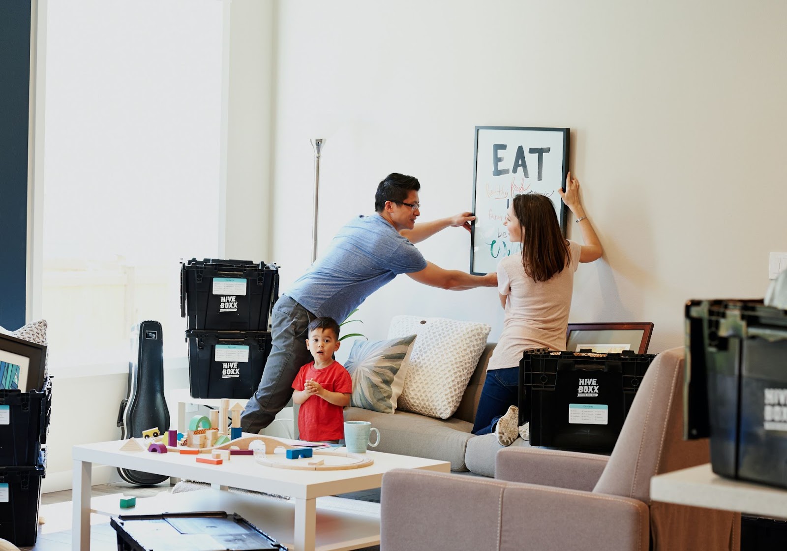 kid playing while mom and dad hang picture frame 