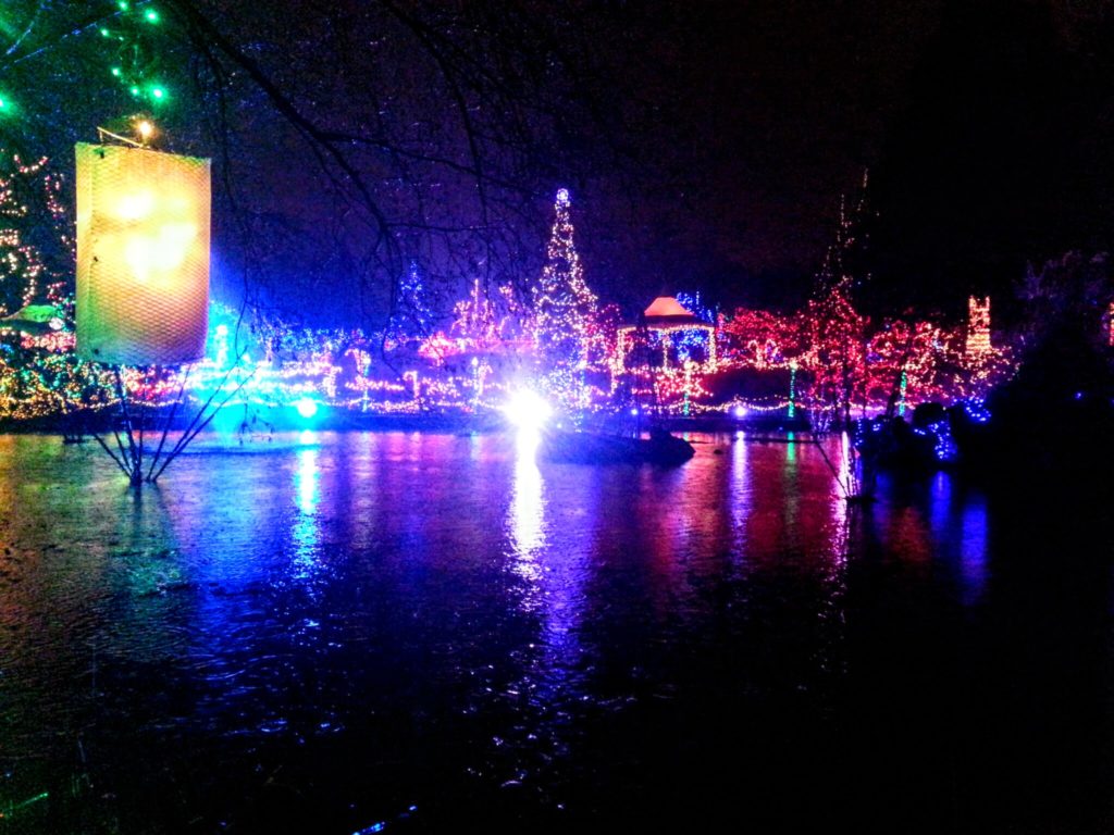 VanDusen Garden festival of lights.  In the background, there are tons of lights covering trees, a pergola, light poles and more.  In the foreground, a lake which is reflecting the lights.  