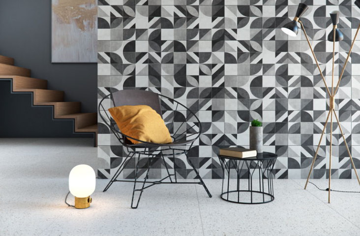 Ambiente com parede com revestimento em preto e branco, piso de porcelanato imitando granilite, poltrona e banquinho de ferro pretos.