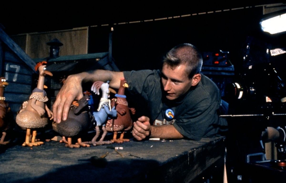 Behind the scenes of Chicken Run: an animator wearing a black t-shirt in the Aardman studios moves some of the stop motion chicken models on a table, they are about the size of his hand.