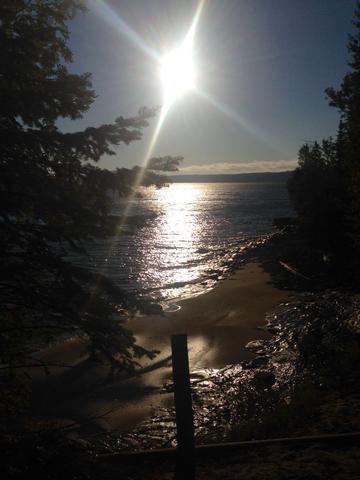 A stunning view of the sun over the water framed by pine trees during my backpacking trip through the UP.