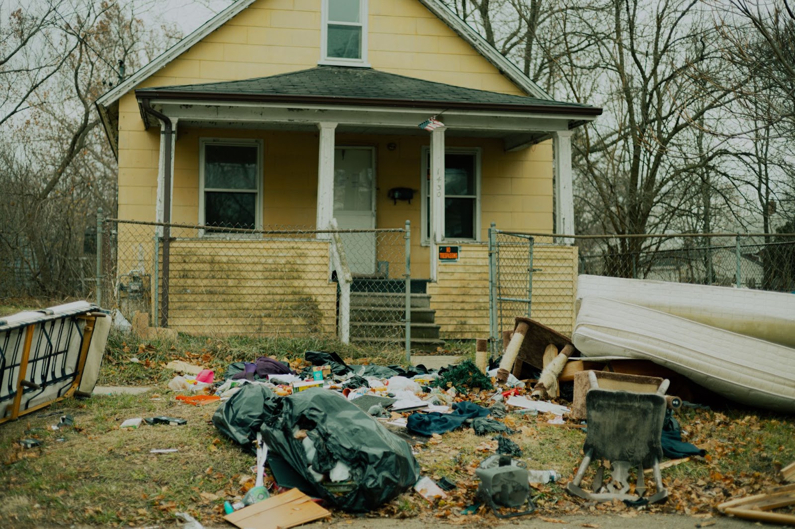 single family, 1.5 story abandoned yellow house with ton of trash in the front yard 