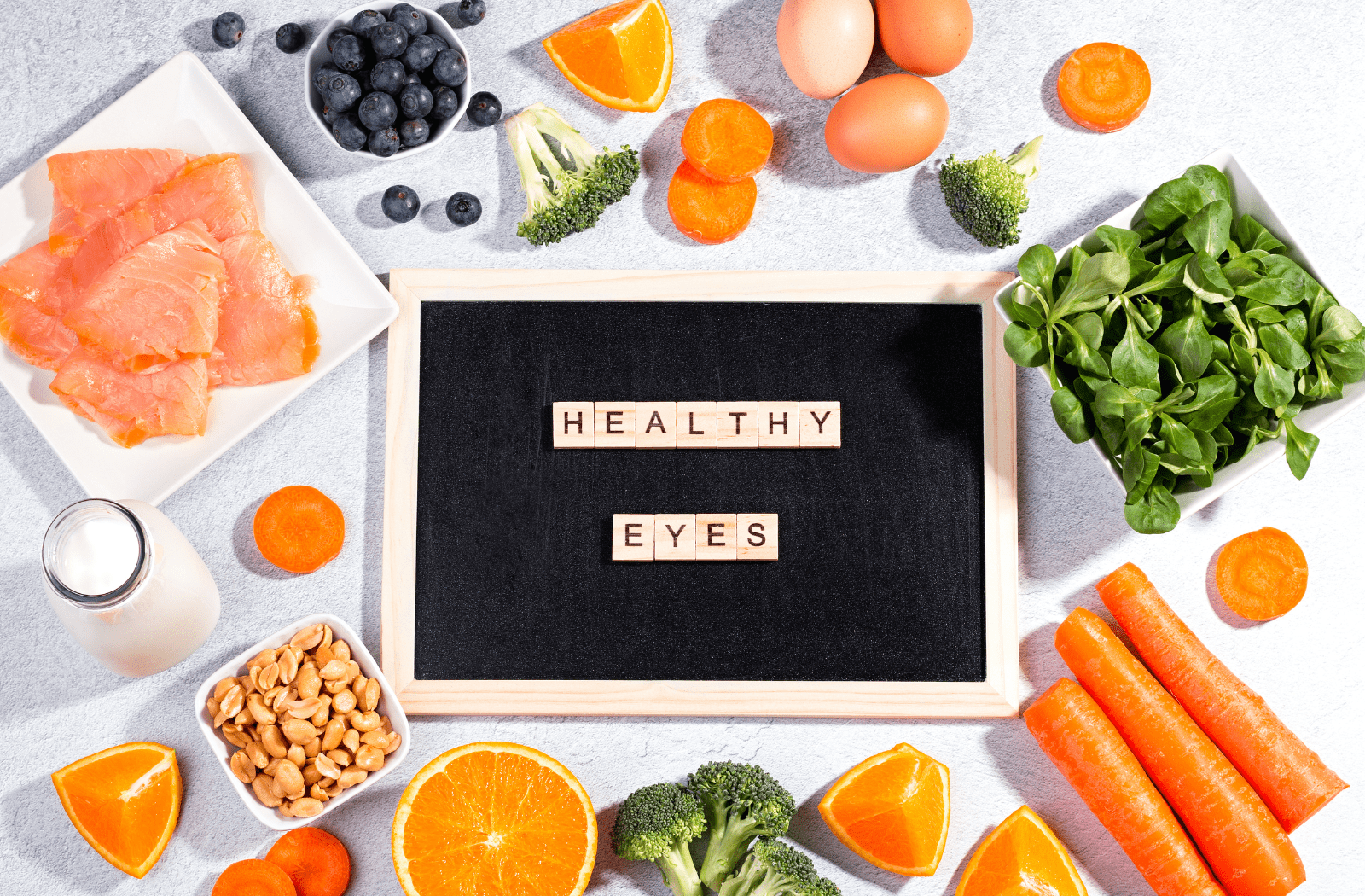 A sign with lettered tiles across it, spelling out "healthy eyes," surrounded by foods like spinach, fish, milk, carrots, oranges, blueberries, and more