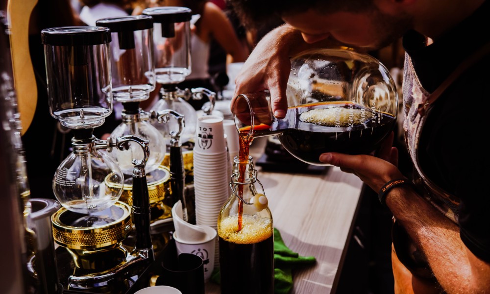 Image of Caucasian male coffee roaster pouring cold brew coffee into glass bottles