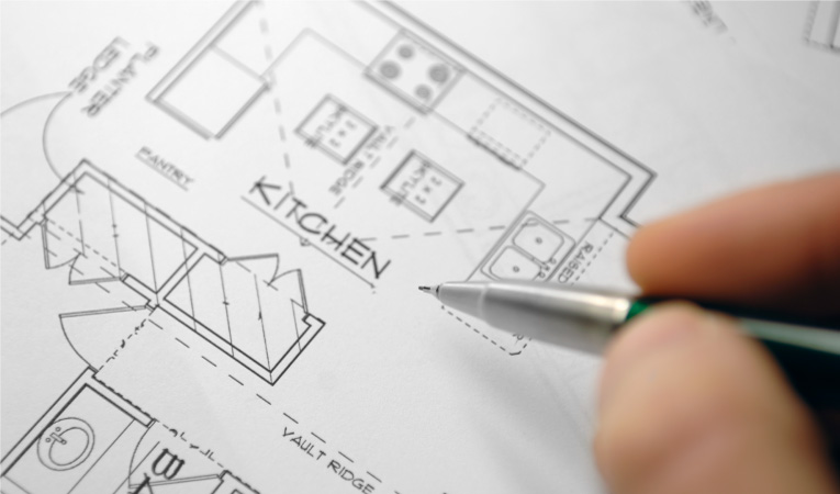 A person writing on a blueprint for a U-shaped kitchen
