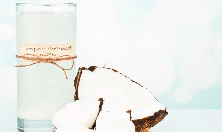 The photo shows a glass of coconut water and a coconut next to it.