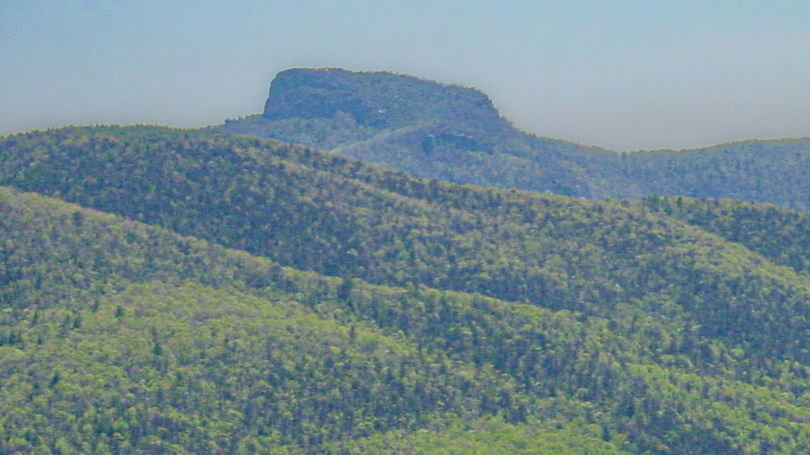A mesa style peak of a mountain surrounded by green fields. 