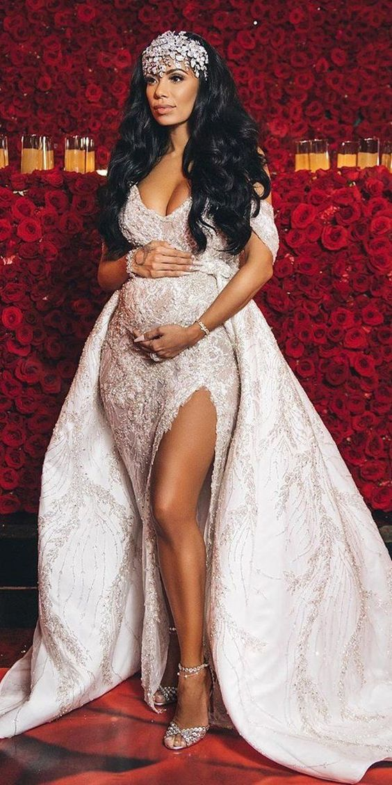 A beautiful bride with a tiara on her head, and a slit wedding gown that shows her bump