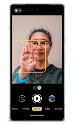 Image 4: 一部 Google Pixel 手機的相機應用界面螢幕上顯示了一位戴眼鏡的女性，正對著鏡頭舉起手掌相機應用啟用了自拍模式，畫面中央有一個黃色的方框，對準了她的手掌下方的相機應用界面顯示了不同的模式選項，包括「Motion」、「Portrait」、「Camera」、「Video」和「Cinematic」，目前選擇的是「Camera」模式，並且設定了三秒的倒數計時