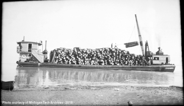 Greyscale historic photo of boat carrying logs