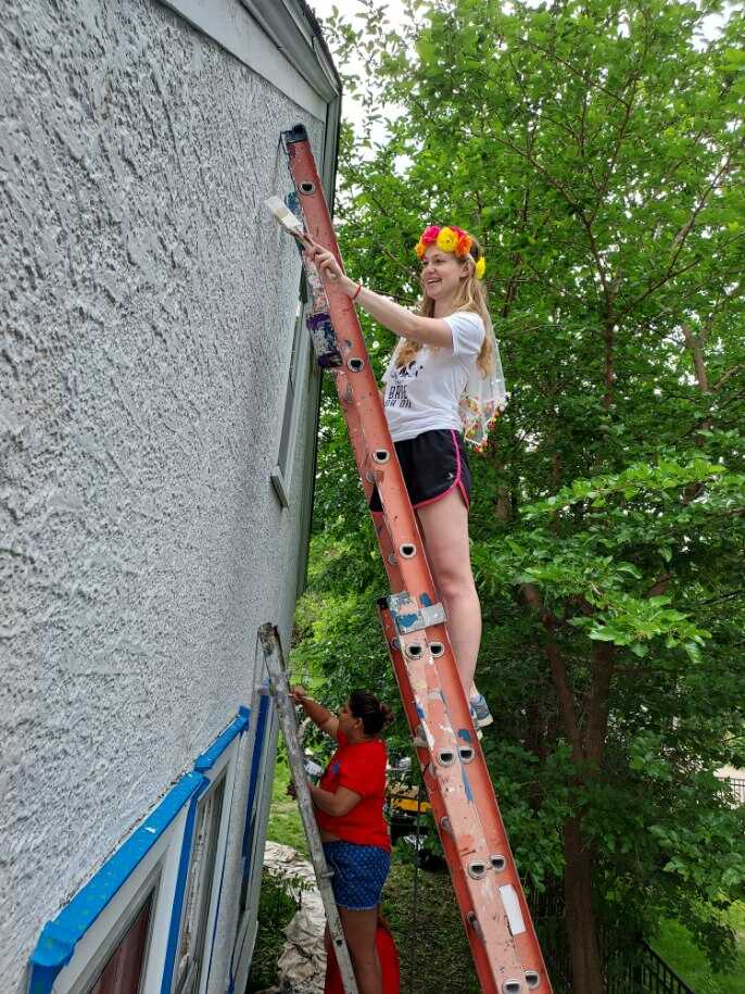 Tori Vogel on ladder a painting house with flower crown 