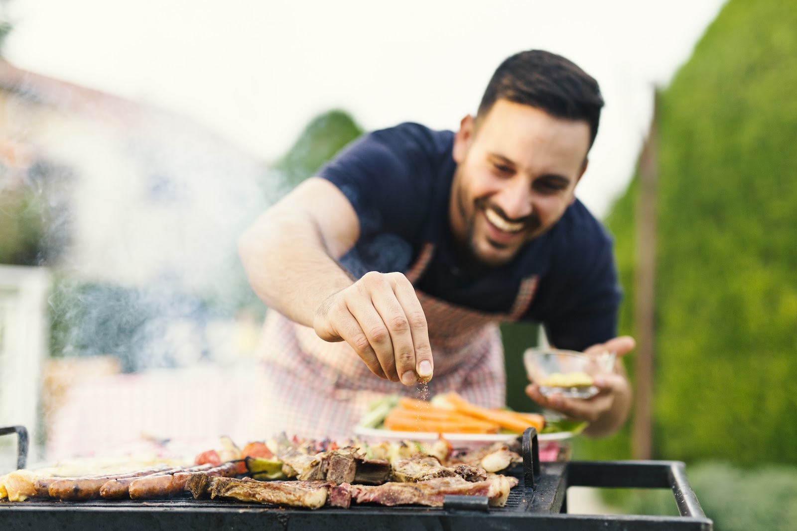 A man smiling while adding spices to grill