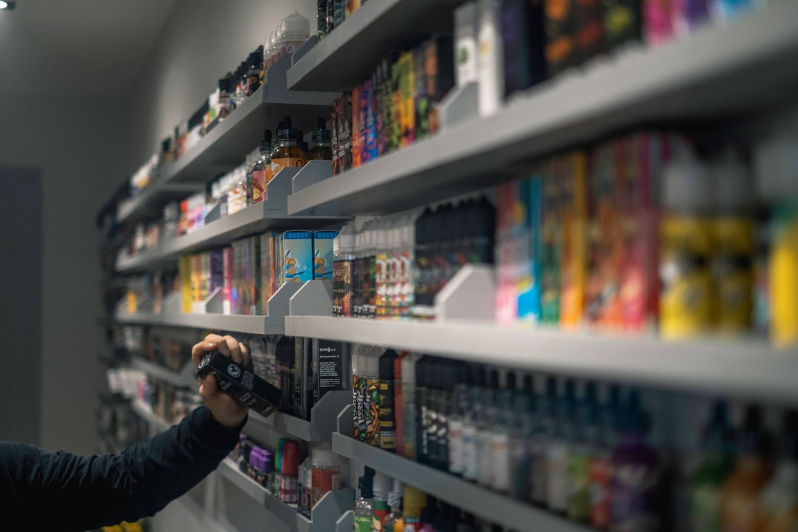 A hand picking out a vape from a shelf of vapes