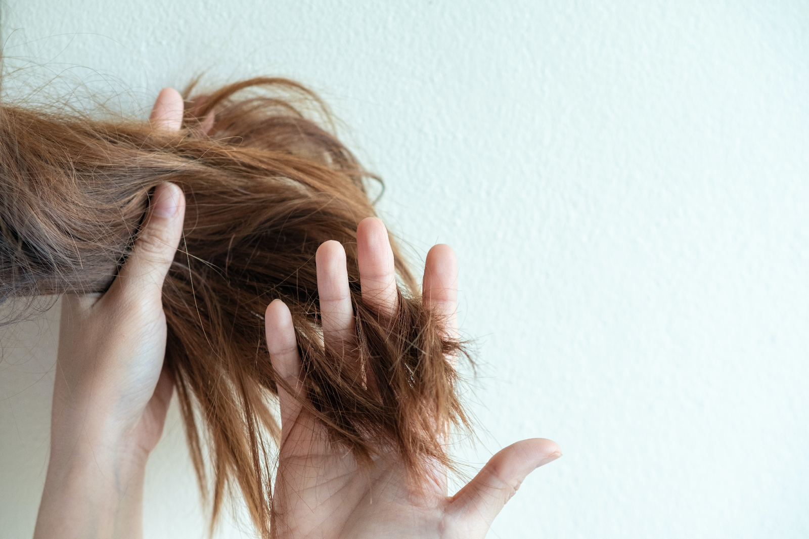 mulher passando a mão entre os fios de cabelo para checar a queda dos fios