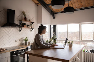 Side view of young female in casual clothes typing message on laptop while sitting at wooden table in kitchen