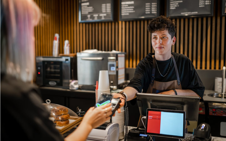 A barista holds out a card reader while a woman pays for her coffee at a local coffee house.