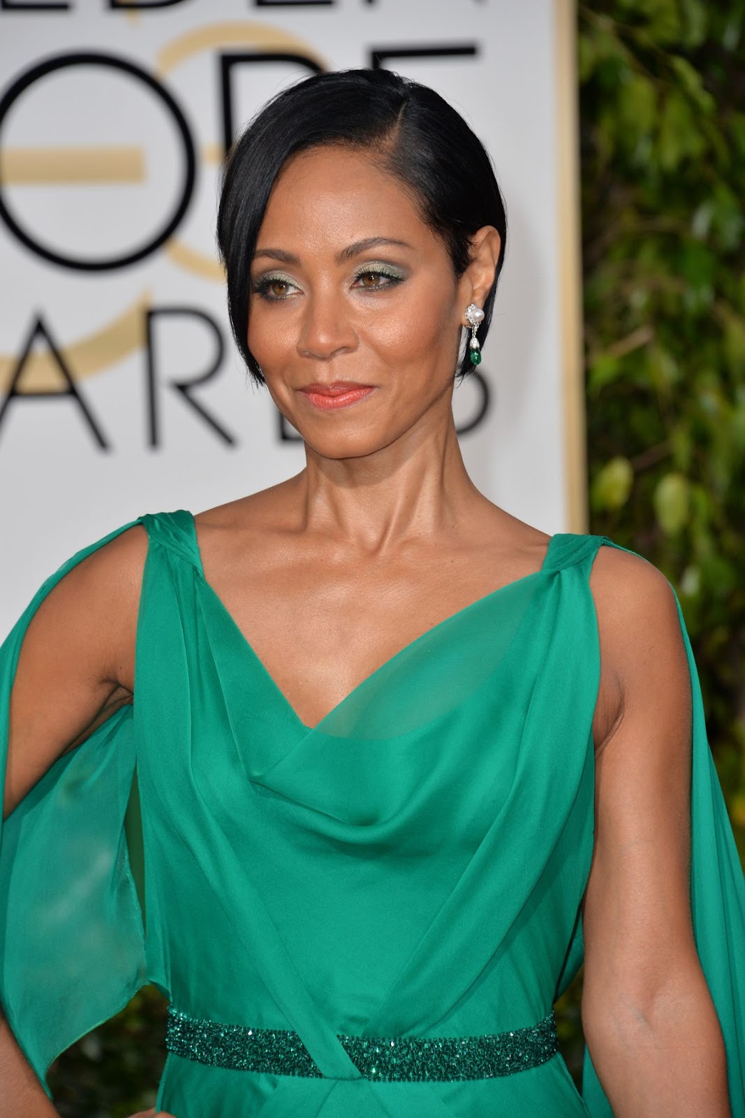 Atriz Jada Pinkett-Smith, mulher negra de cabelos lisos e curtos, em um penteado bem preso, ela também usa um vestido verde bem soltinho.