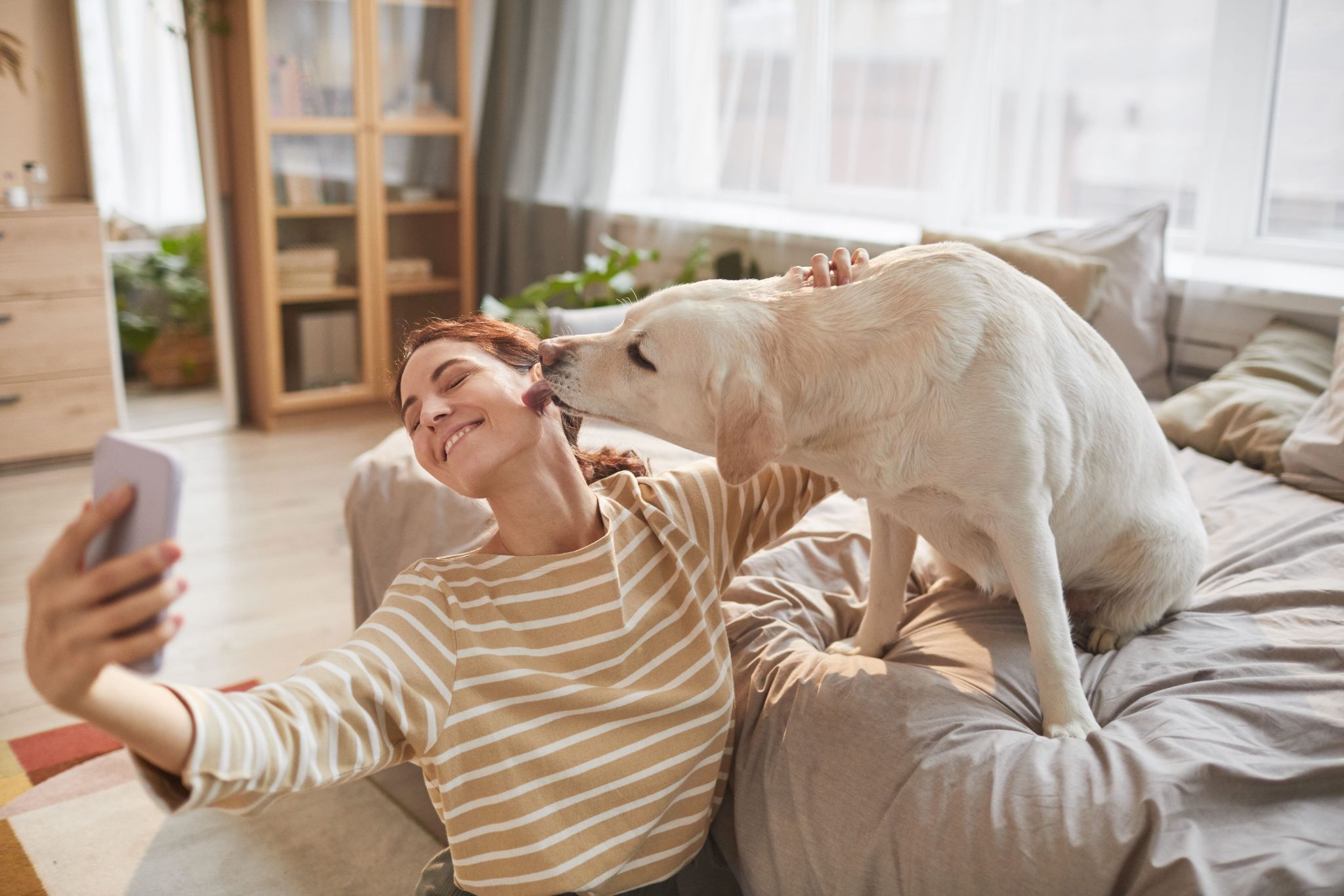 Mulher faz uma selfie sorrindo enquanto cão lambe seu rosto.