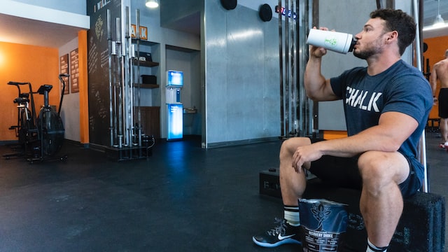 A man sitting in the gym drinking essential amino acids (EAAs) out of his shaker to aid in recovery