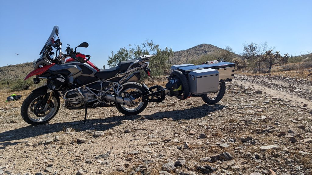 A loaded ADV1 one-wheeled motorcycle trailer being held up by the side stand of a BMW 1250GS