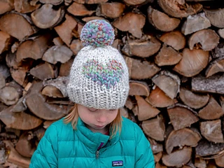 little girl wearing a knit hat with heart-shaped colorwork and large pom