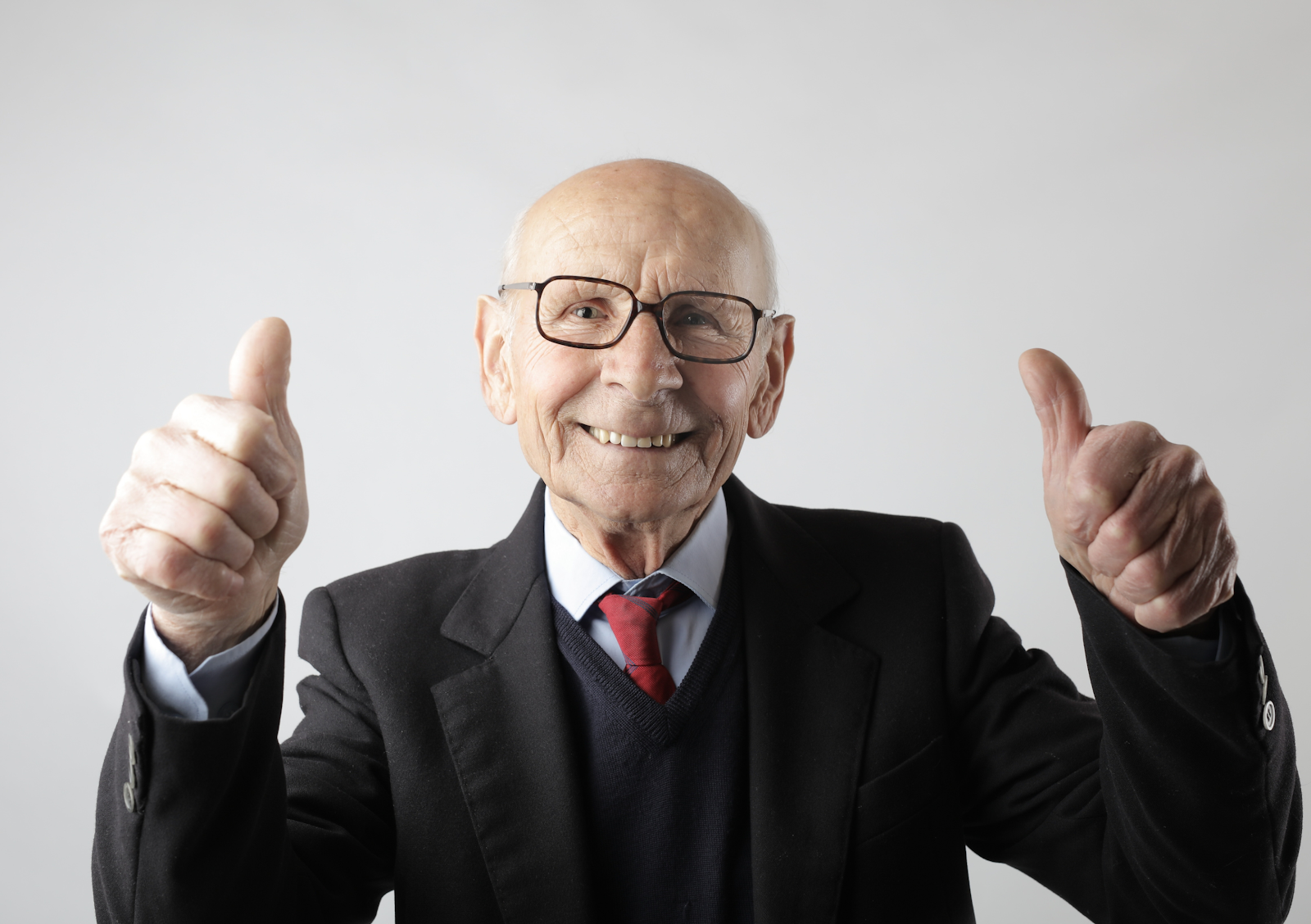 An old man holding his thumbs up while smiling.