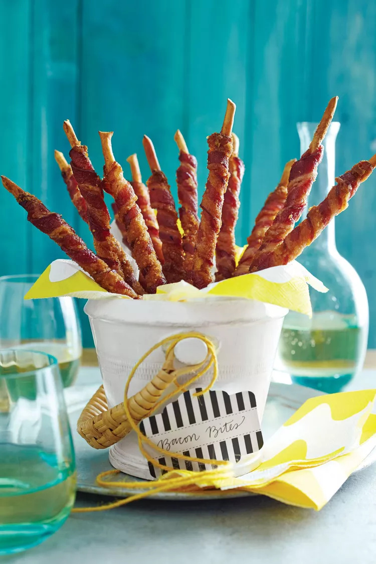 A bucket filled with crispy bacon-wrapped breadsticks, labeled 'Bacon Bites,' standing against a vibrant blue background, perfect for a savory snack display.