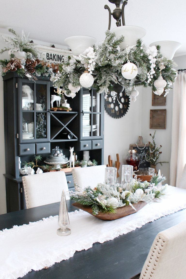 dining room table with chandelier that is strung with pine garland and white christmas ornaments. 